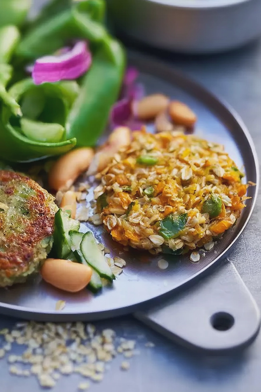 Hafer-Gemüse-Bratlinge auf einem Teller, serviert mit buntem Salat und frischen Kräutern.