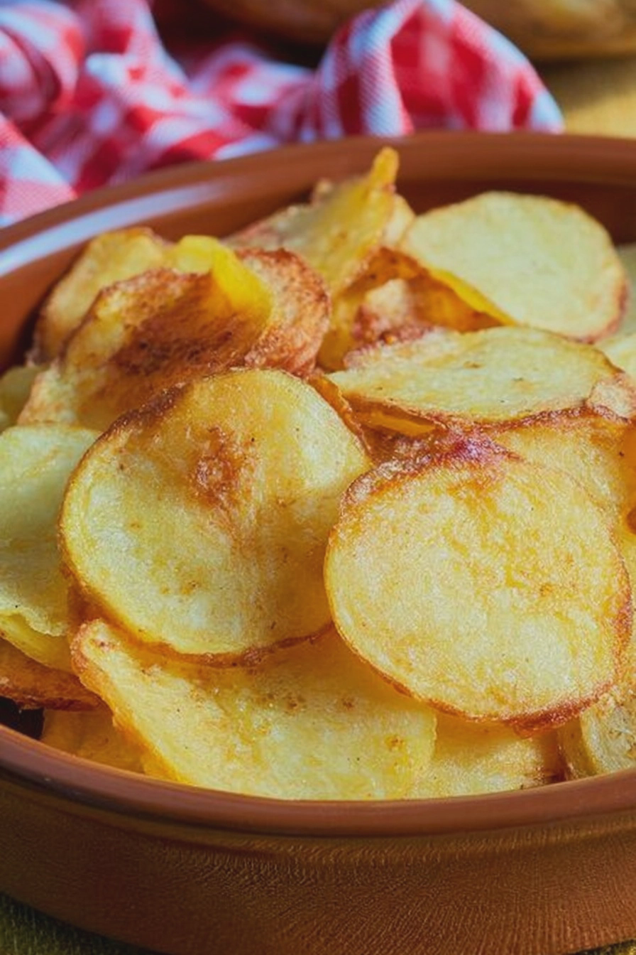 Knusprige Kartoffelchips aus der Heißluftfritteuse auf einem Holzbrett mit Salz.
