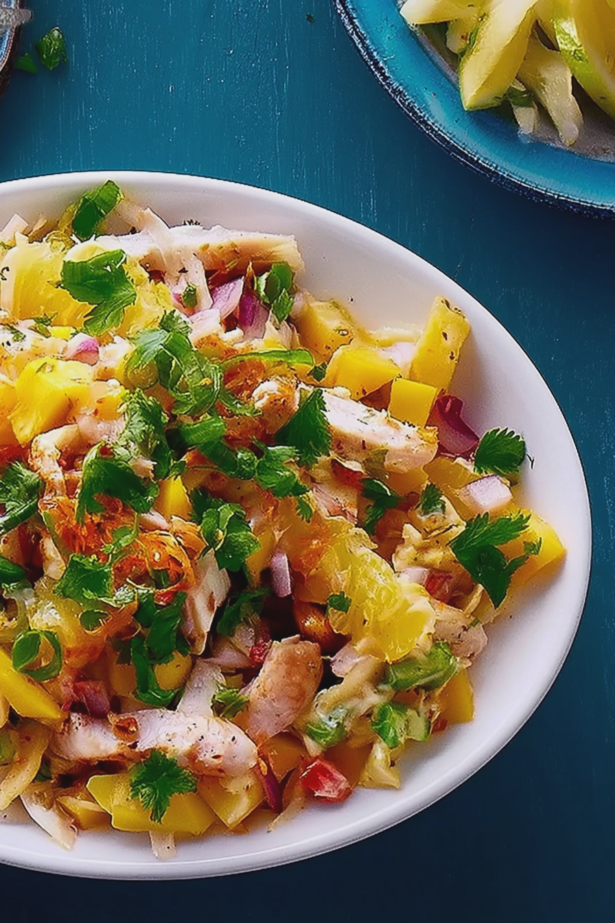 Zitronen-Mango-Hühnchensalat auf einem Servierteller, dekoriert mit frischen Zitronen- und Mangostücken.